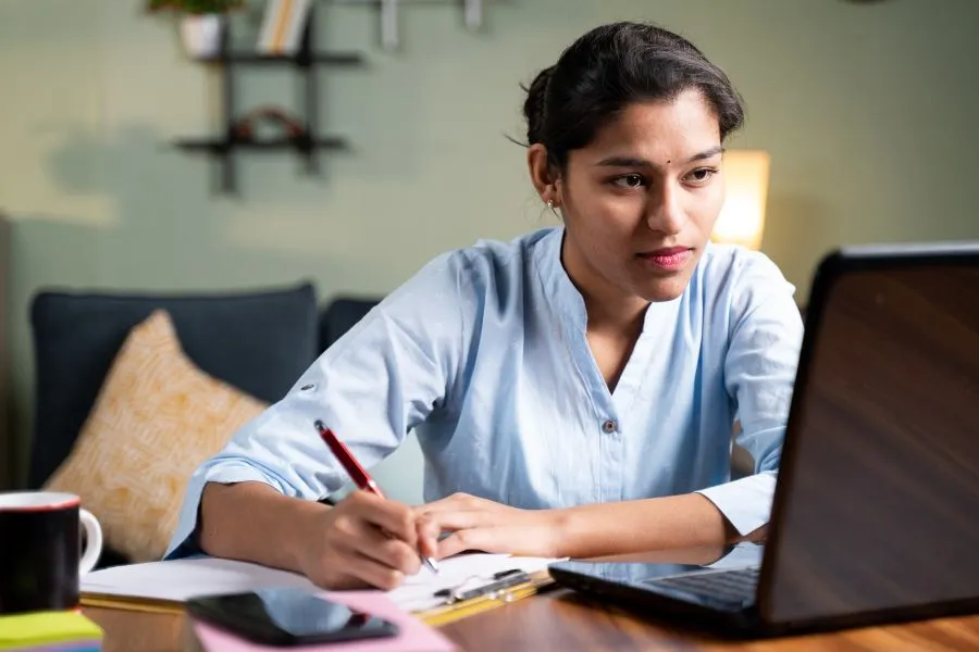 Young business woman writing down notes by looking laptop