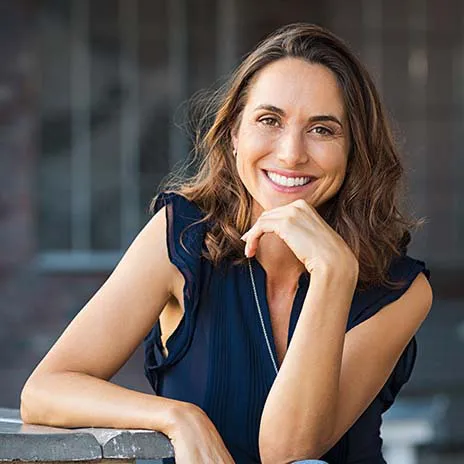 a woman sitting down with her hand under her chin smiling