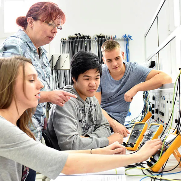 Instructor working with students on electronic testing equipment in a lab setting.