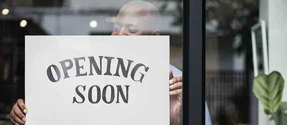 An opening soon sign hangs on the inside of a business window