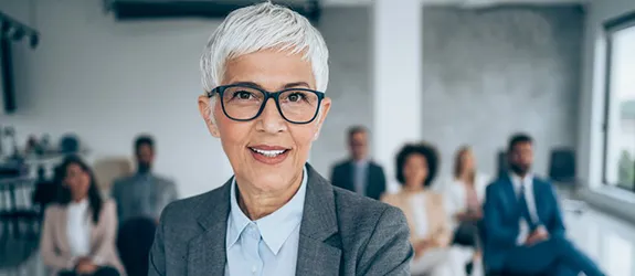 A teacher smiles at the camera as their class is seated behind them