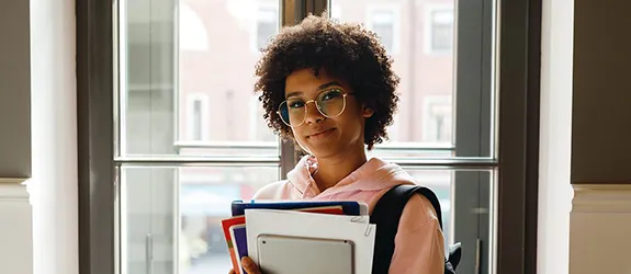 A student holds books and notebooks on campus