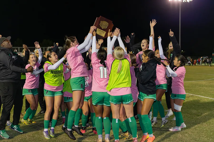 womens soccer team celebrating the championship win while holding up a trophy
