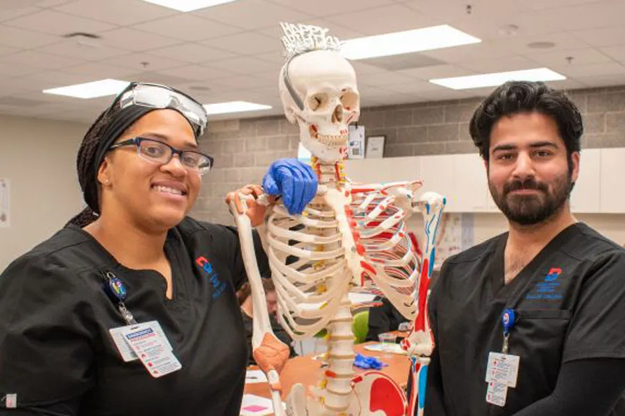 Two Occupational Therapy students stand next to a skeleton in their class.