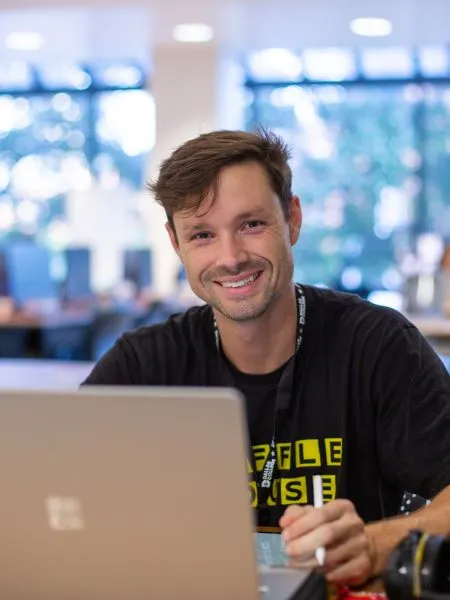 A student sits at a desk in the El Centro library, looking up from his laptop.