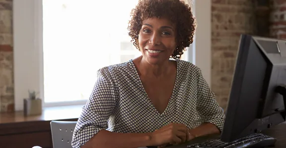 An adult student smiles from behind a computer