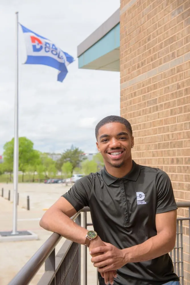 Student stands outdoors in front of a Dallas College flag