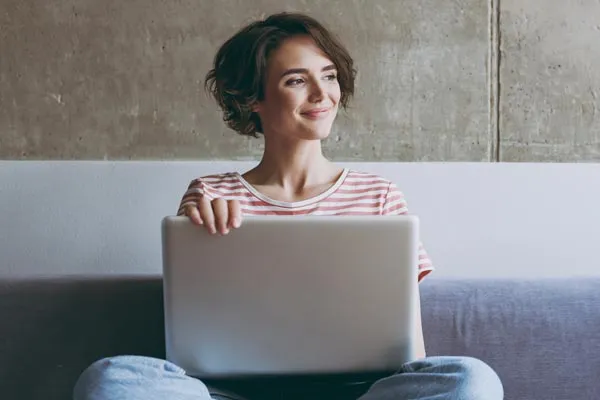 A female student sites with a laptop open in her lap while she looks away