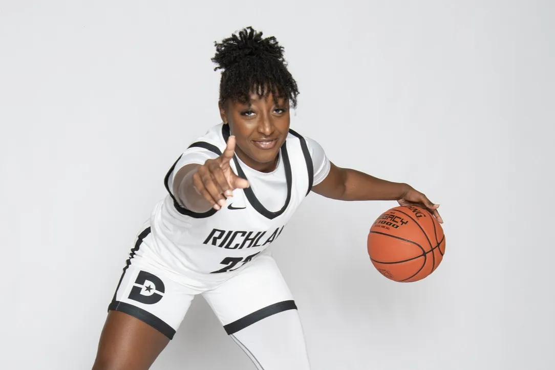 A Richland Women's Basketball player dribbles the ball and holds up a finger