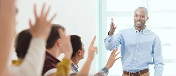 A teacher motions for their adult students to raise their hand