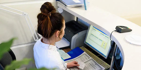 An office worker sits at the front desk of their office and looks at a computer and over the counter