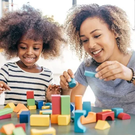 A teacher and student play with wooden blocks at a table