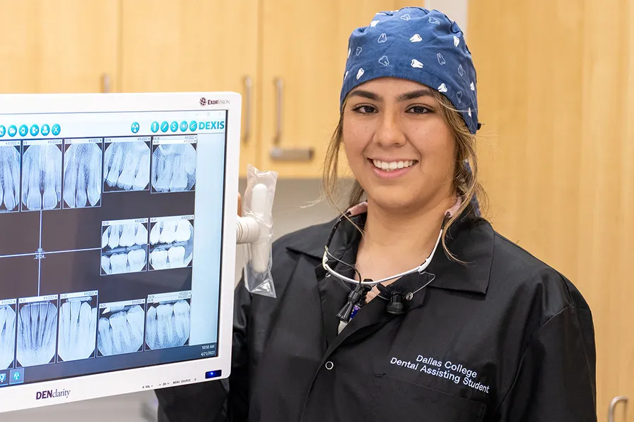 A Dental Assistant student stands next to an xray of someone's mouth