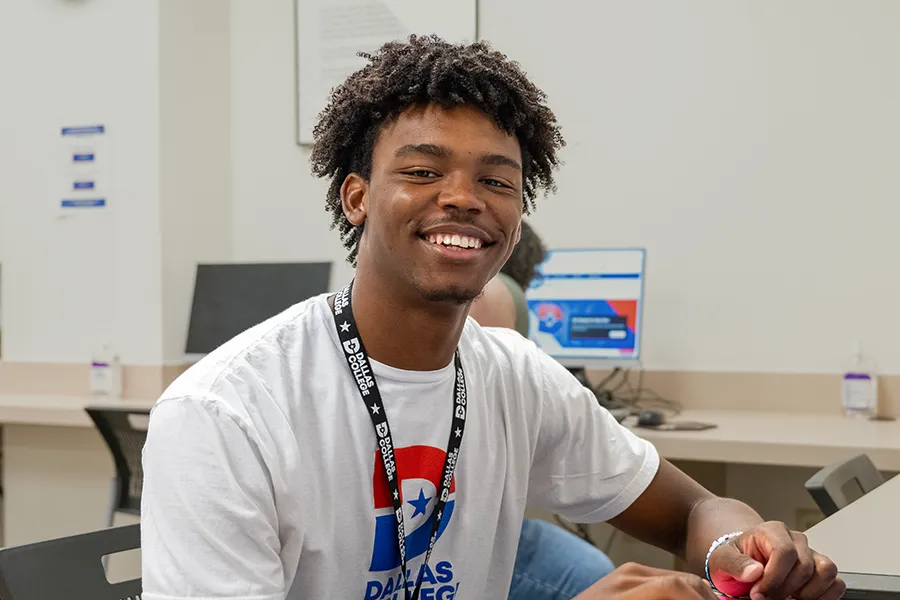 Student wearing a Dallas College tshirt sits at a computer in the computer lab