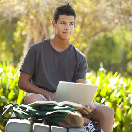 A student sits outside with an open laptop in his lap