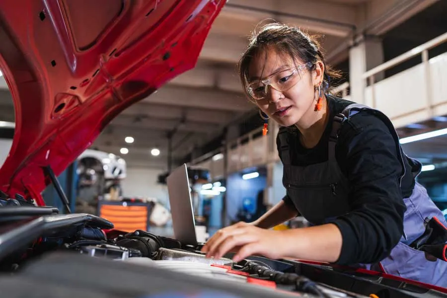 An auto mechanic student looks under a car on a lift.