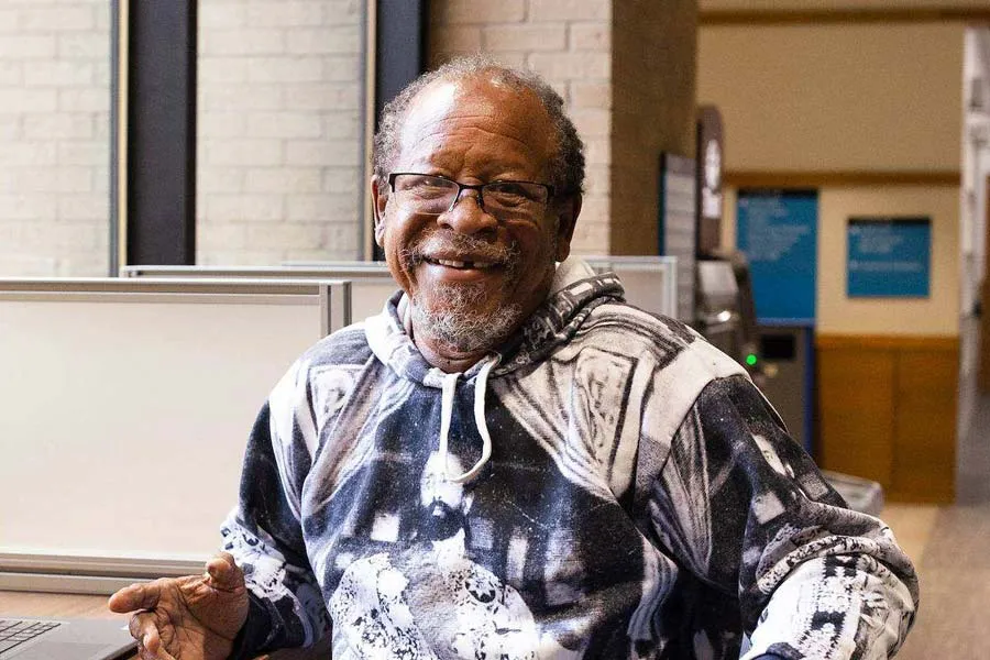 A lifelong learning student sits in the hallway at Eastfield at a study spot and turns to smile at the camera