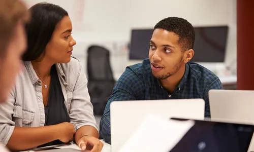 Students talk while sitting at desk in a computer lab