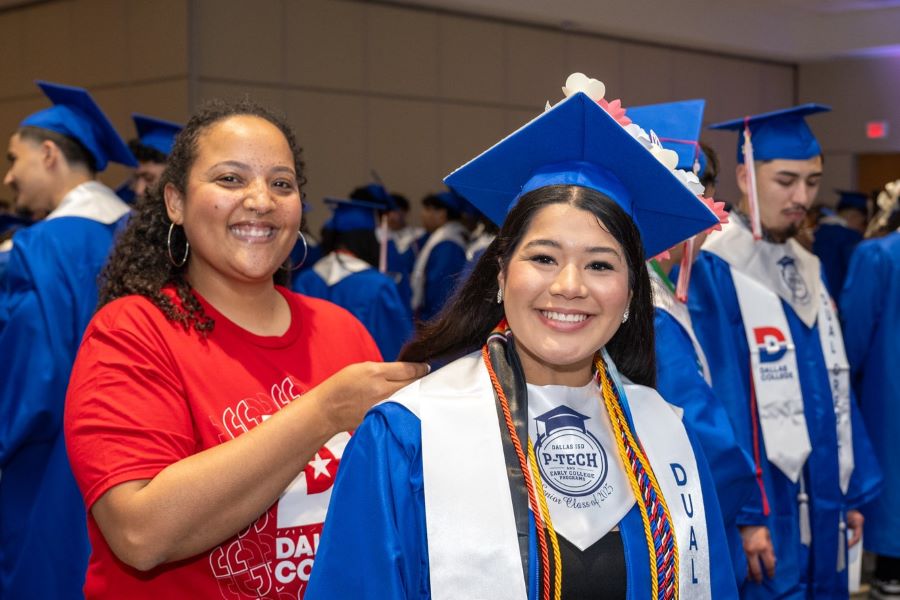 An employee helps a student with their graduation gown
