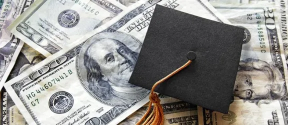 A graduation cap rests atop a pile of cash