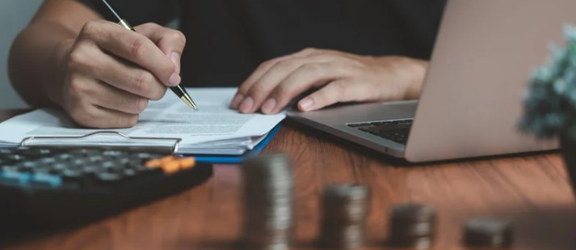A student writes at a desk with stacks of coins in front of them