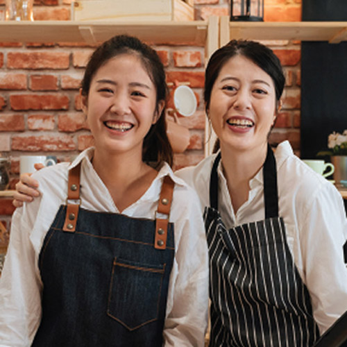 Two people wearing aprons standing together in a café or bakery kitchen.