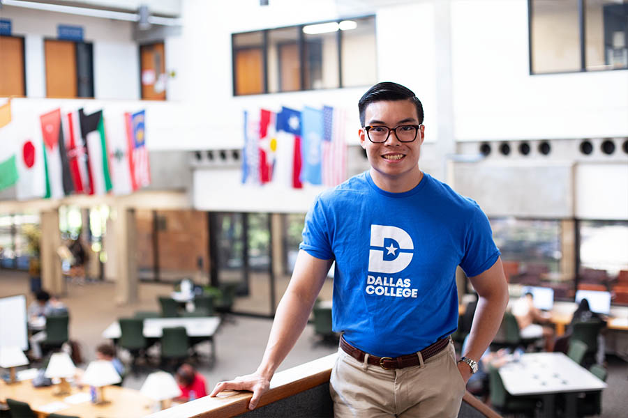 Employee at Dallas College wearing a t-shirt stands in a library filled with international flags