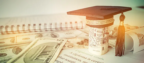 Money is spread across a tabletop and a graduation cap sits on top