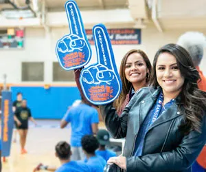 Fans of Eastfield athletics hold up large foam hands with the #1 sign at a volleyball game