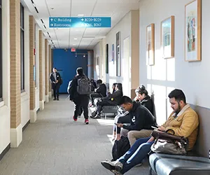 Students sit and look at books and phones in a long hallway at El Centro