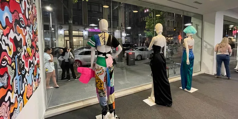 Mannequins with student fashion stand in front of a large window lining the street
