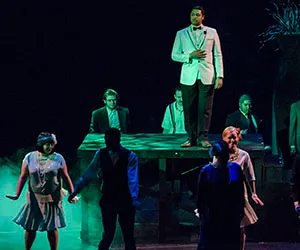 Eastfield students perform a theater production on a dark stage with a green light falling on the cast