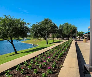 A view of the North Lake campus showing a walkway, flower garden and lake