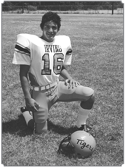 Ray Cerda in Irving High School football uniform, posing on football field with one knee down and helmet out in front.