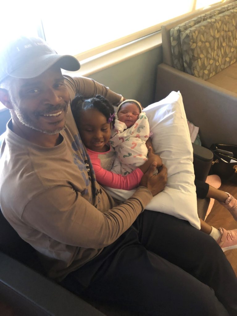 Richard Miles sitting on sofa holding his two young daughters.