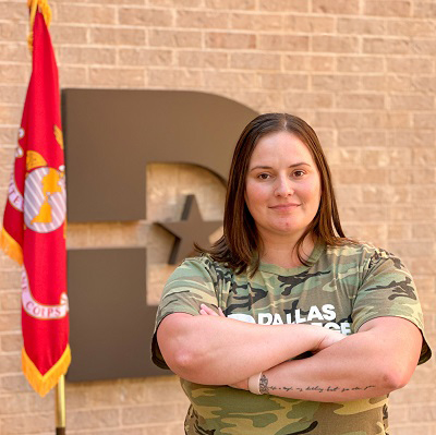 Jaqueline Shorter poses in front of Dallas College D with arms crossed and Marine flag in the background.
