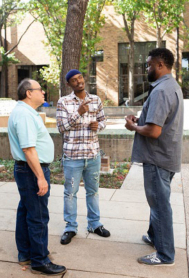 Raymoi Victorine standing outside on campus talking to faculty members.