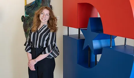 Ava Stipe posing next to Dallas College logo big D.