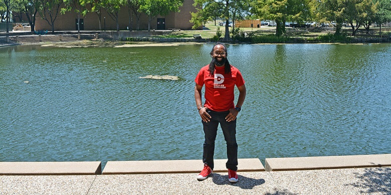 Elgrie Hurd wearing Dallas College t-shirt and standing in front of pond.