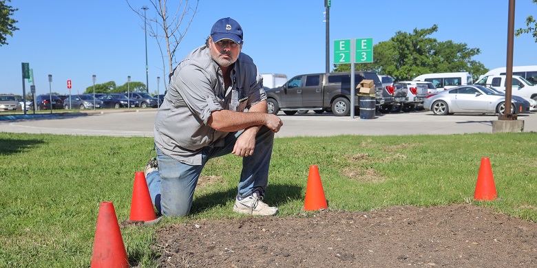 John Racek kneeling near cones marking landscaping for butterfly observation.