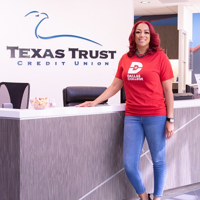 Krystal Hamilton standing in front of desk and Texas Trust Credit Union sign.