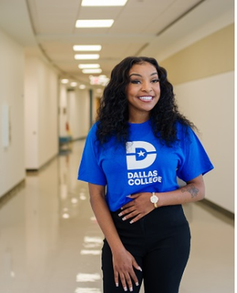 Kianna Vaughn in a blue shirt with a white Dallas College logo is smiling while standing up.