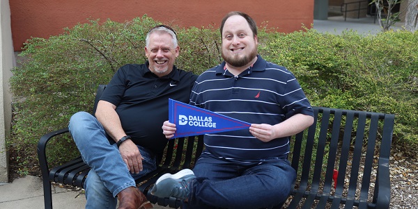 Ken and Joshua Kidd sitting on bench and holding Dallas College pennant.
