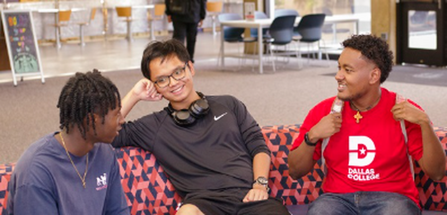 Konata Kidane wearing a red shirt with the Dallas College logo and a backpack sits with two friends on a couch.