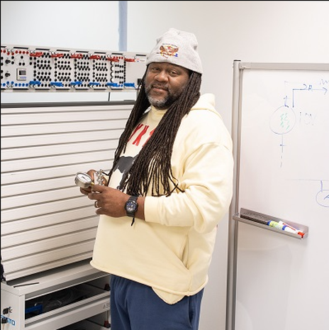 Marcus Russell holding a gauge in a workshop of classroom setting with a whiteboard behind him.