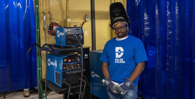 Caleb Lynn standing next to welding equipment, wearing Dallas College t-shirt.