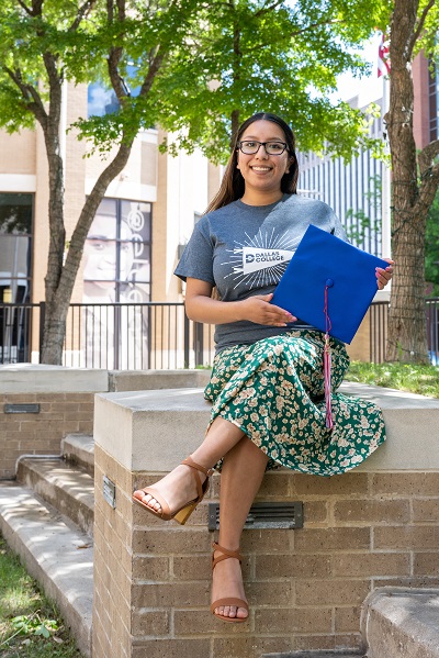 Daisy Donjuan sitting on a wall outside campus holding her graduation cap.