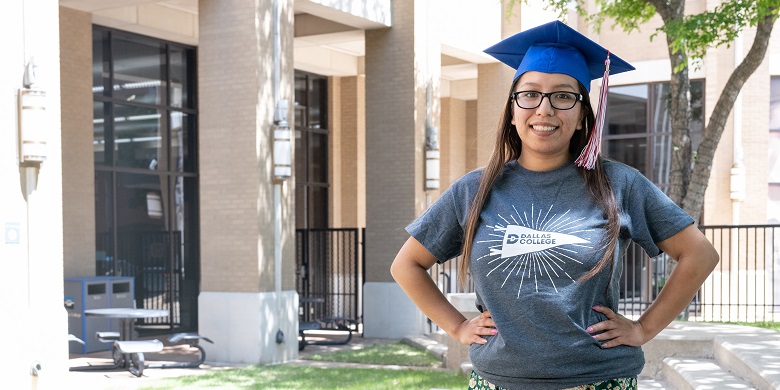 Daisy Donjuan standing in front of campus building wearing a graduation cap.
