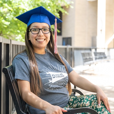 Daisy Donjuan sitting on bench, wearing graduation cap.