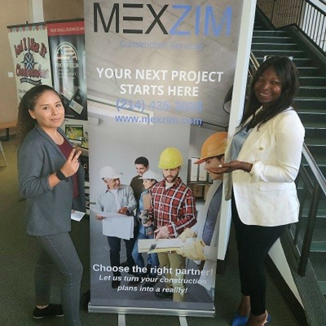 Ebbah and another Dallas College student in professional attire standing beside a promotional banner for Mexzim Corporation, a Dallas-based construction services company.
